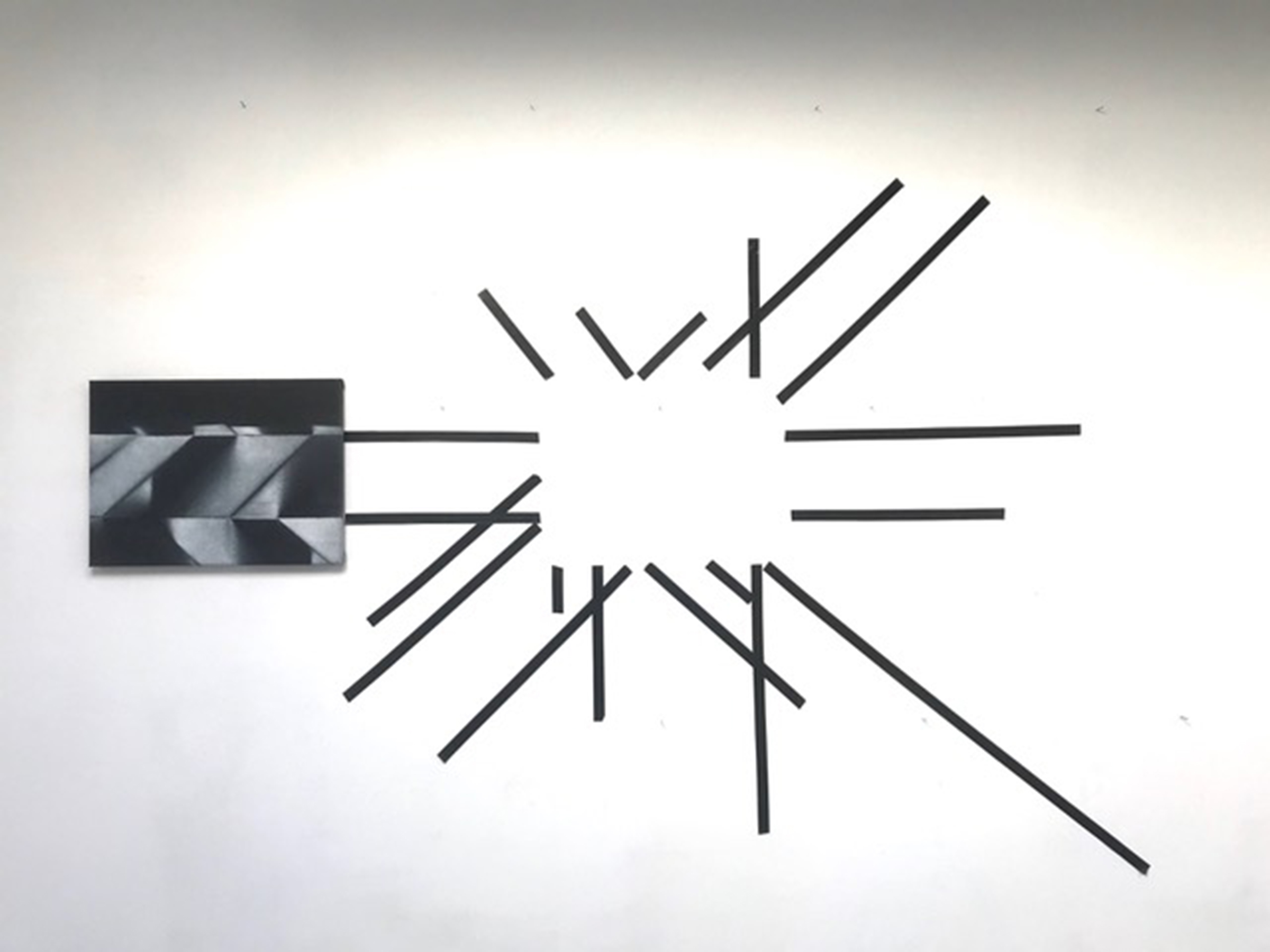 zwarte lijnen op de muur creeren een wit rechthoekig vlak in het midden, uiterst links hangt een schilderij met geometrische vormen